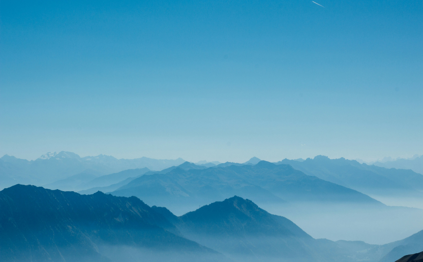 Paesaggio di montagne sfumate nel blu sotto un cielo azzurro limpido, simbolo di calma, introspezione e spiritualità.