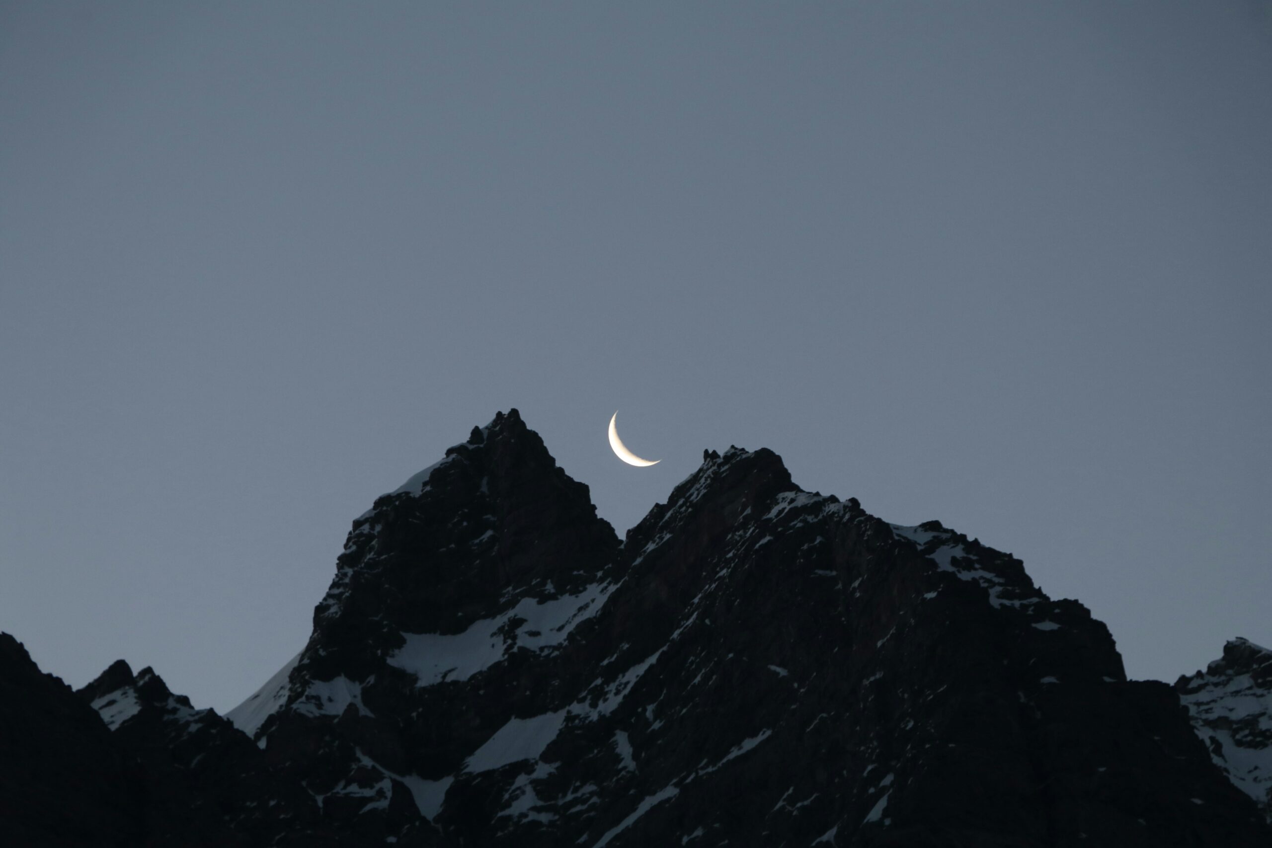 Luna crescente tra due montagne scure al crepuscolo, simbolo di mistero, interiorità e significato spirituale del colore nero.